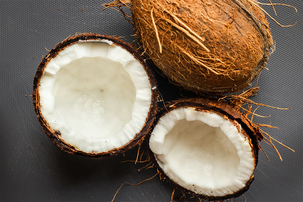 Pair of coconuts with one cut in half showing what makes coconut milk, a dairy alternative.