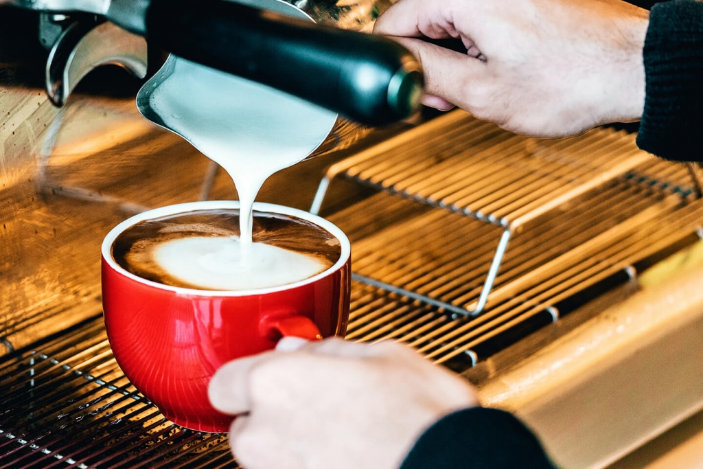 Barista adding milk to an espresso beverage.