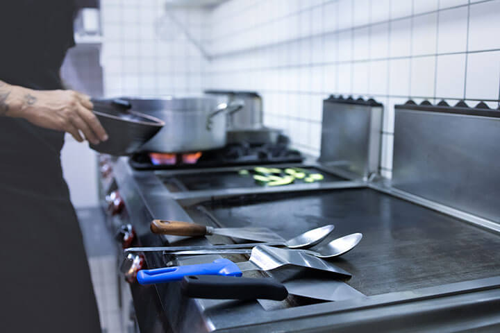 A flat top grill in a commercial kitchen. Shown with utensils. 