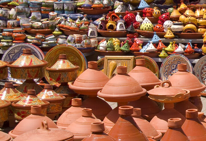 Traditional earthen clay tagine pots and lids at a market in Marrakesh, Morocco mirror the clay architecture of Aït Benhaddou.