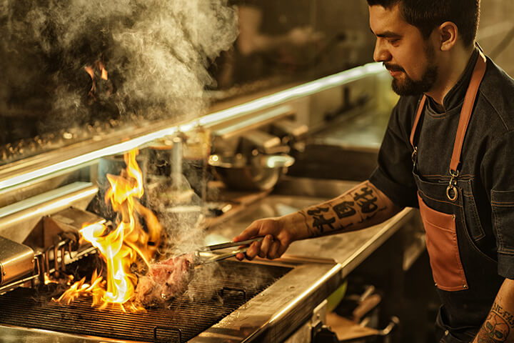 Pro chef cooking on a gas stove with flames.