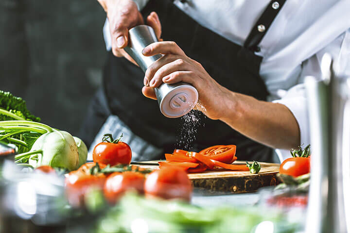 Chef adds salt to sliced tomatoes. 