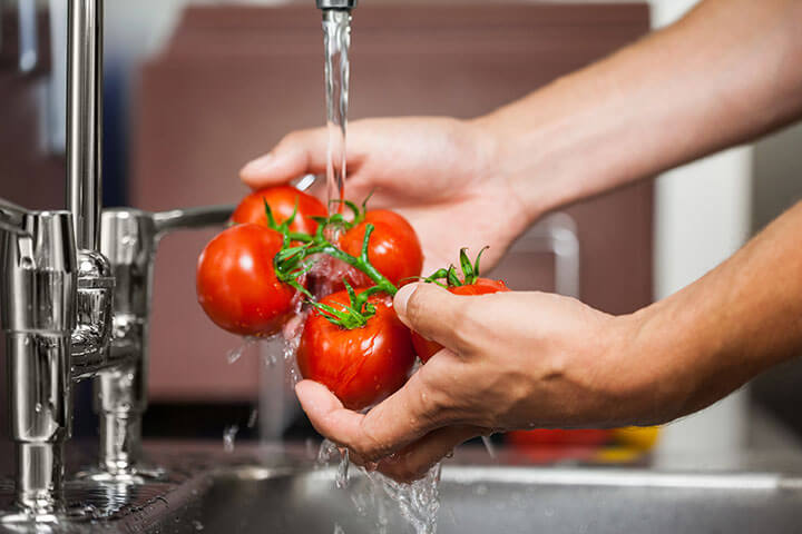 A chef washes fresh, whole tomatoes under running water. 