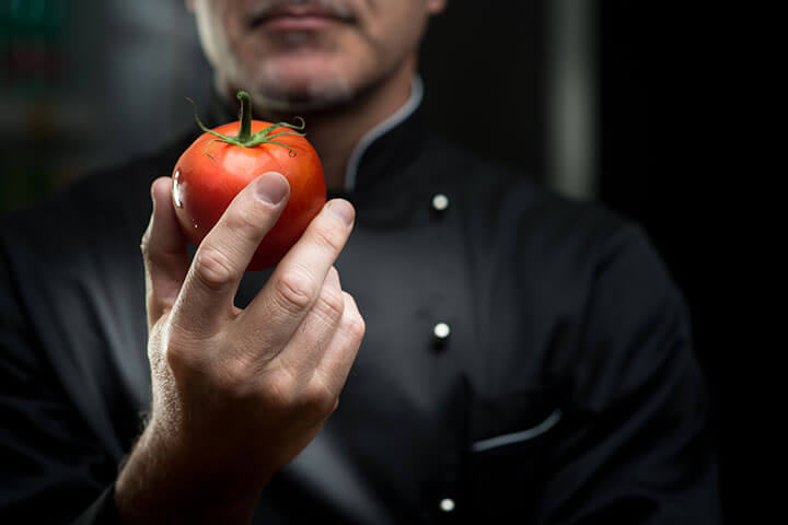 A chef stares at a tomato in an almost hypnotic state; perhaps in awe, perhaps in fear of bacteria.