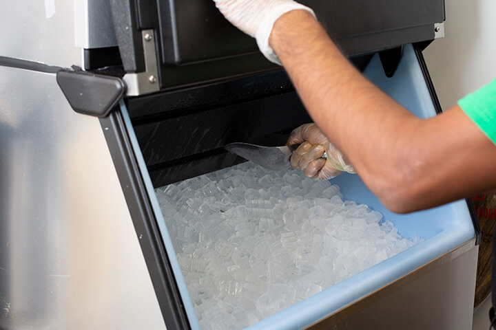 A commercial ice machine with an employee using gloves and a scoop.