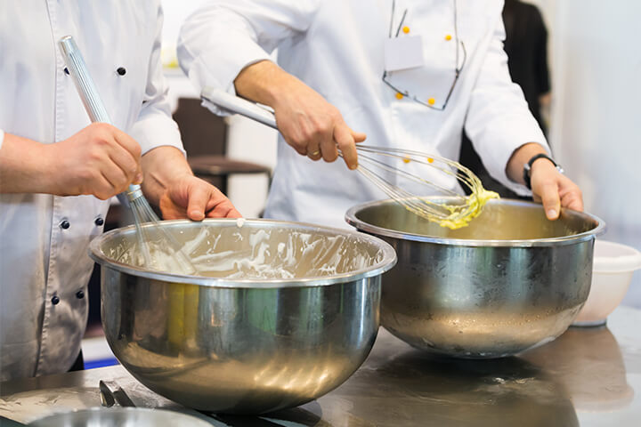 Two chefs whip desserts with balloon whisks. 