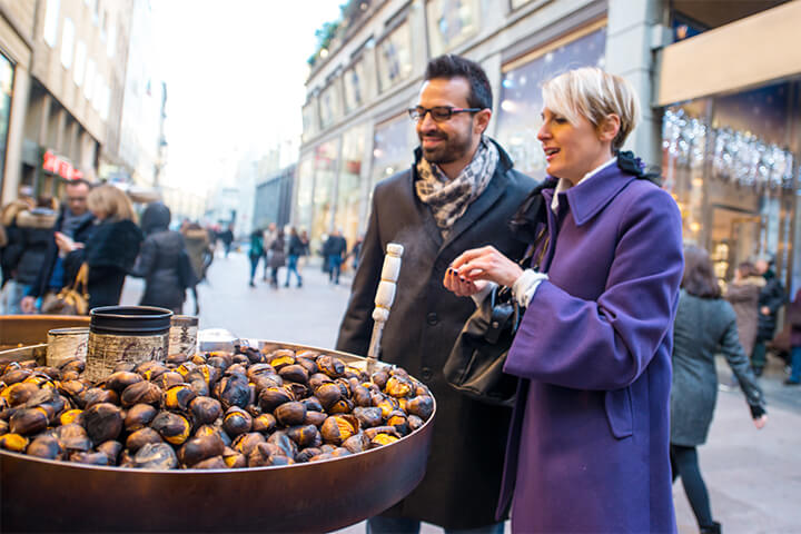 A couple in Milan decides to purchase roasted chestnuts after being drawn in by their smoky, sweet, and nutty aroma.