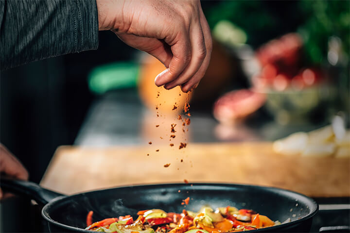 A chef sprinkles spices over food.