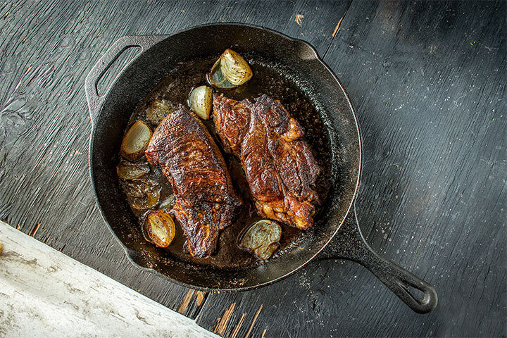 Seared steak with large garlic cloves in a cast iron pan.
