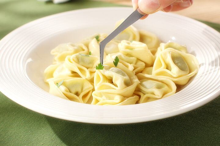 Image of a chef using tweezers to add herbs to pasta. 