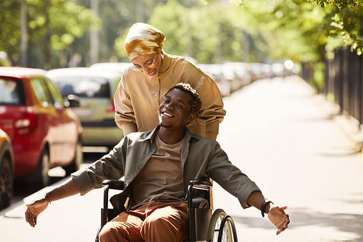 A woman pushes a happy man in a wheelchair.
