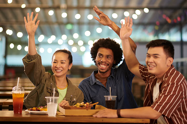 Three friendly people raise their hand..