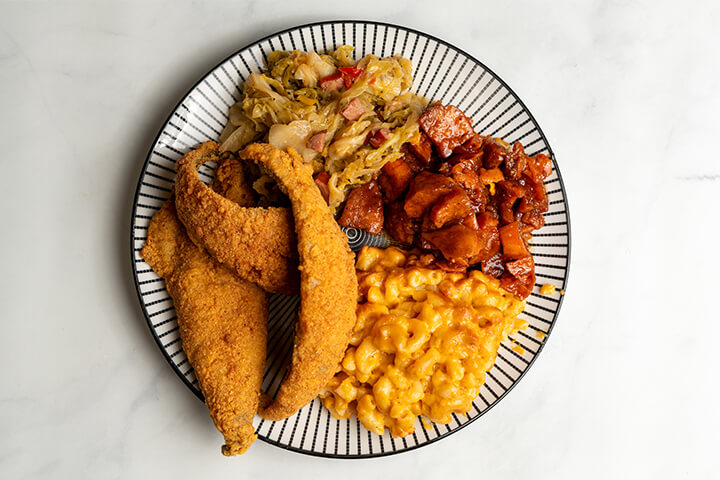 A plate of soul food featuring staple foods like fried catfish and mac n' cheese.