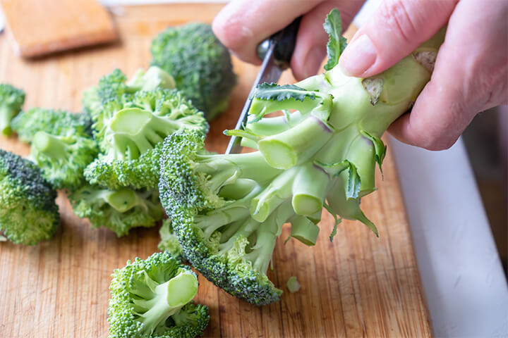 A person cuts florets off a broccoli stalk.