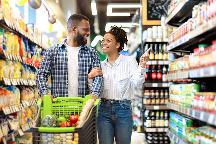 A happy couple stroll down a grocery store aisle.