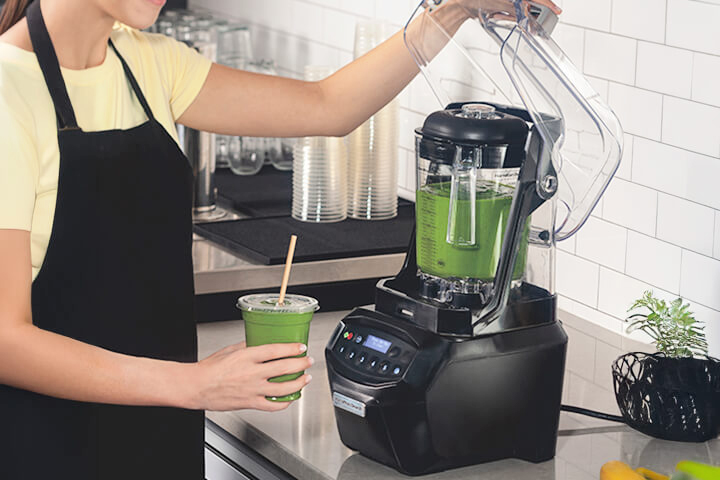 A woman makes a green smoothie using the Summit Edge High-Performance Blender by Hamilton Beach Commercial.