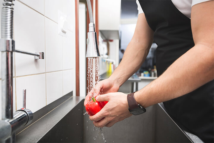 A restaurant employee washes a tomato in a sink.