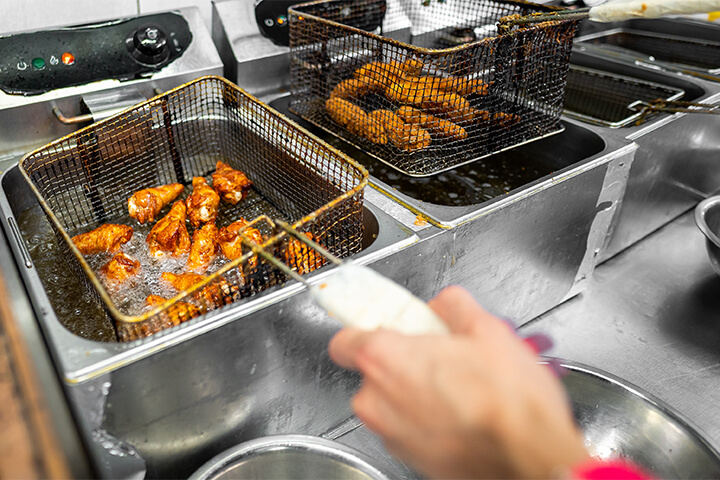 A person prepares fried chicken in a commercial kitchen.