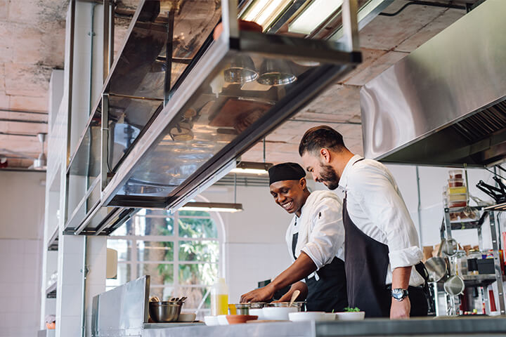 Two friends work in a kitchen.