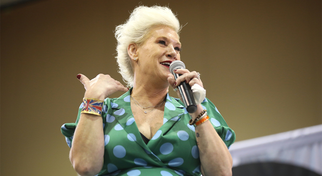 Anne Burrell, American chef and television host. She is smiling and talking into a microphone, wearing a green blouse with white polka dots.