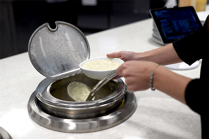 A person helps herself to some food that is heated in a drop-in induction well by Vollrath.