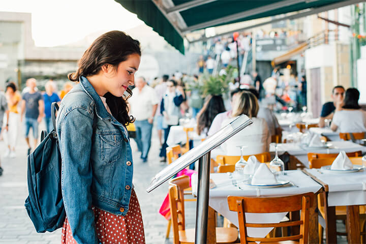 A woman reads a menu posted outdoors. 