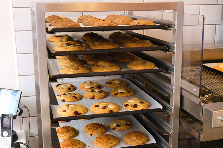 Cookies cooling from the oven in a commercial setting, still on their parchment paper and sheet pans. 