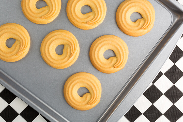 Cute baked goods on a solid sheet pan above a checkered design. 