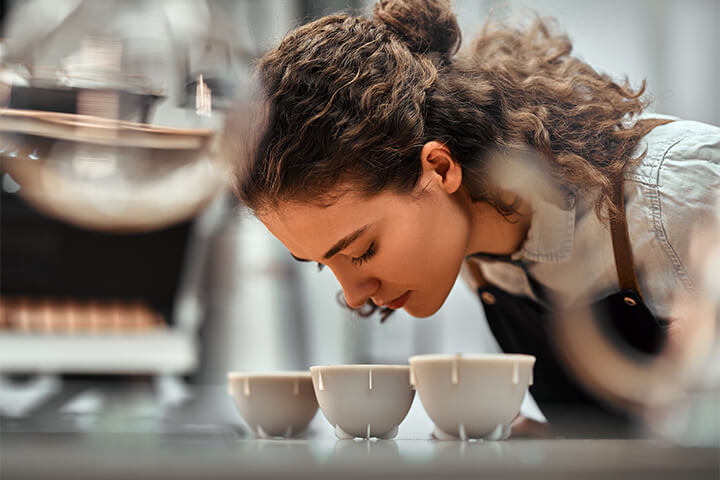 A young woman smells coffee.