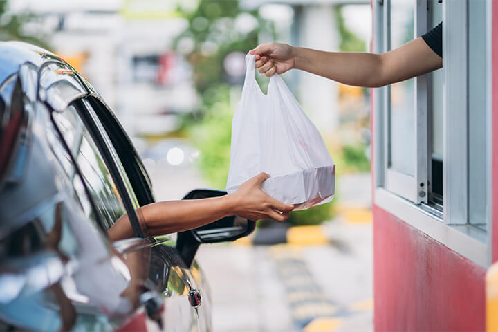 A drive-up take-out customer is handed a plastic bag.