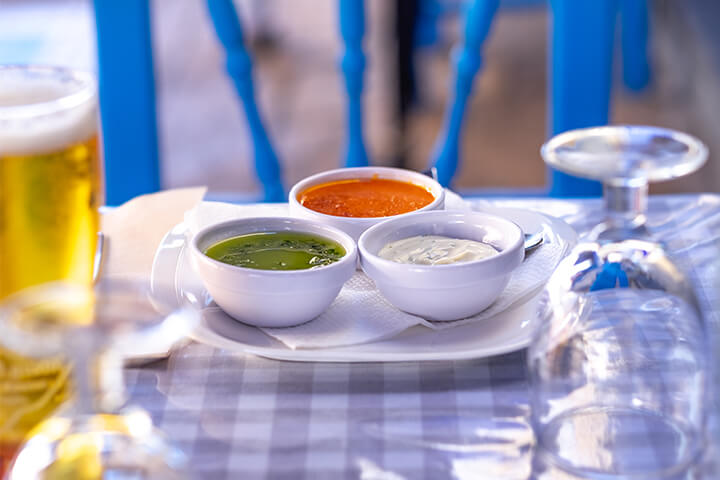A set table with three sauces, an upside-down water glass, and a beer.