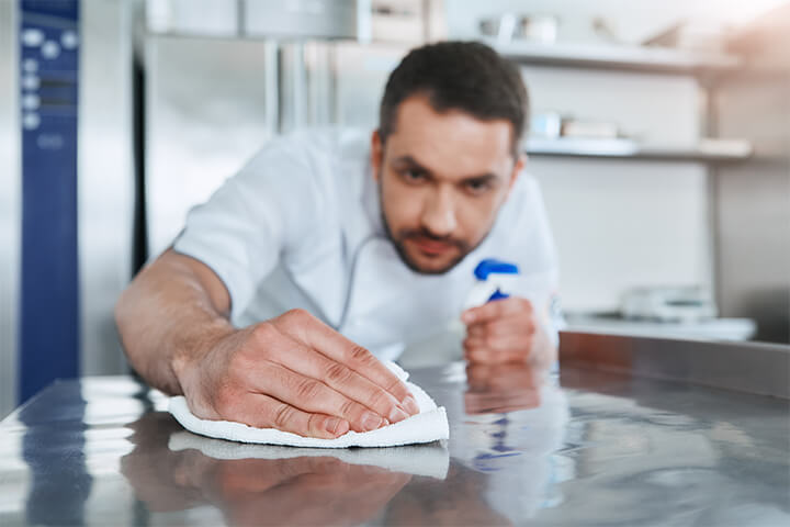 A man sanitizes a surface in the kitchen. 