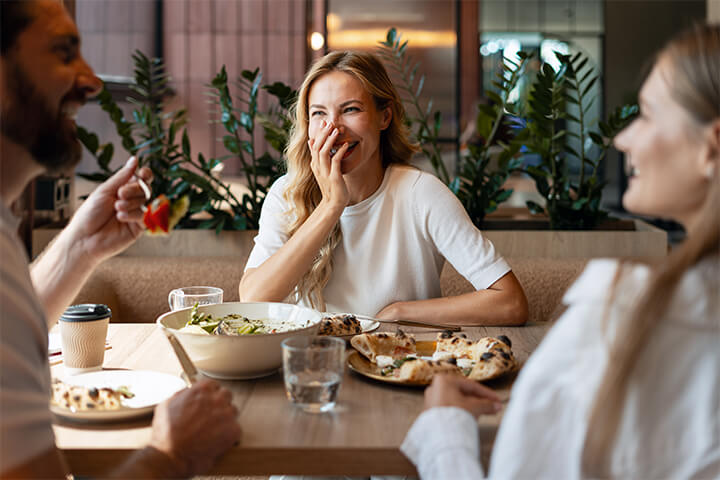 A group of three friends laugh at dinner.