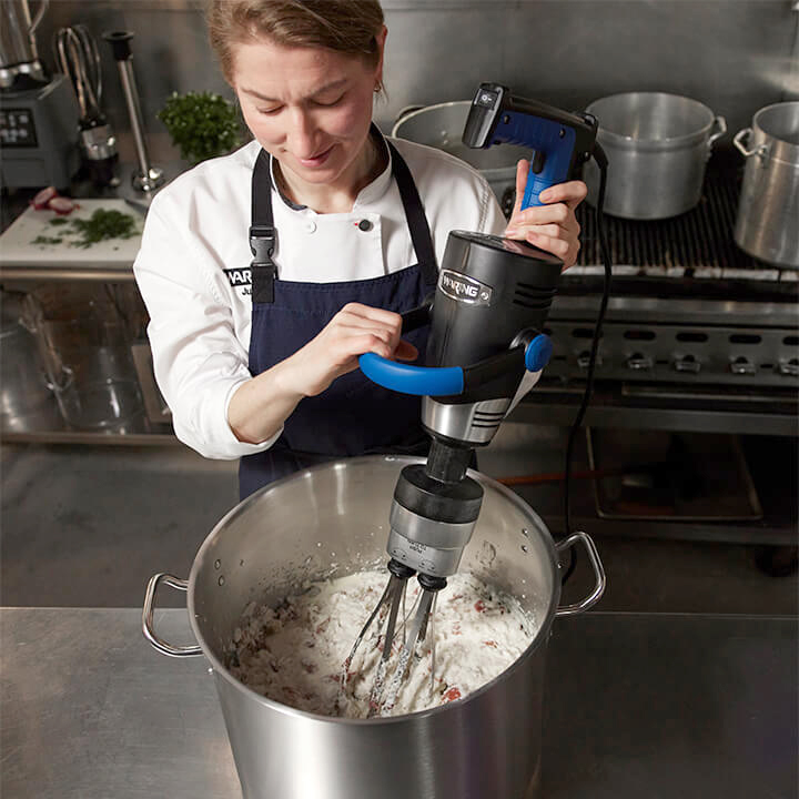 A chef operates the immersion blender using the optional whisk attachment. 