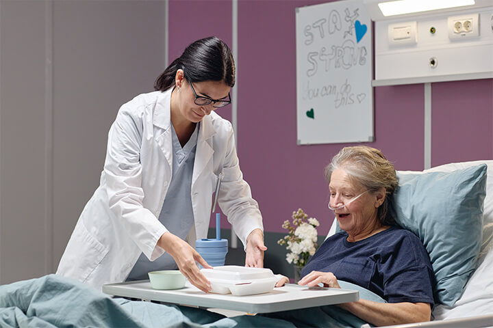 A doctor serves a meal to an old, happy woman.