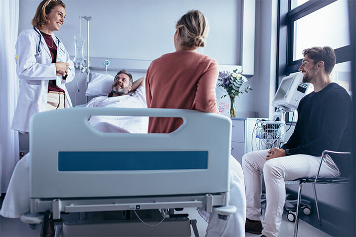 Friends, a doctor, and a male patient are happy in a hospital room.