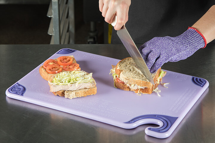A person cuts a sandwich on a purple cutting board.