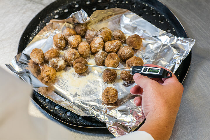 A chef takes the temperature of a meatball.
