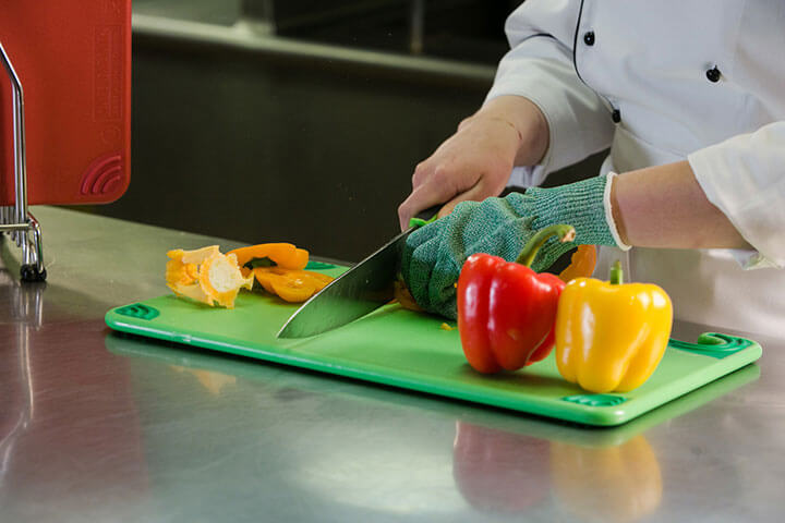 A woman chops vegetables on a green cutting board.