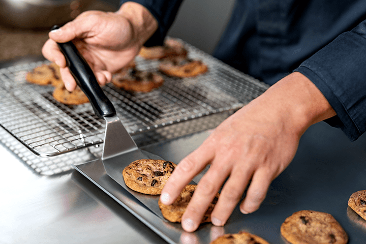 Moving cookies from the sheet pan to the cooling area.